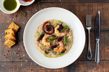 Risotto with jumbo shrimp and octopus on a white porcelain plate on wooden table. Seafood risotto