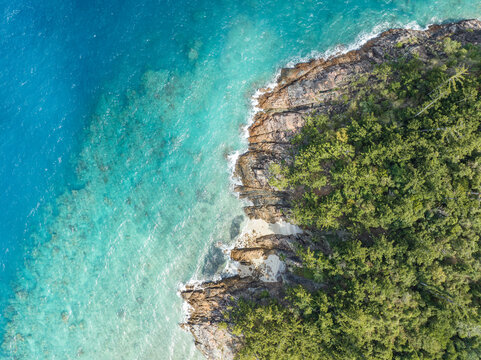 High angle aerial bird's eye drone view of the rocky coastline and tiny beaches on Arkhurst Island, a small islet near Hayman Island, Whitsunday Islands, Great Barrier Reef, Queensland, Australia.