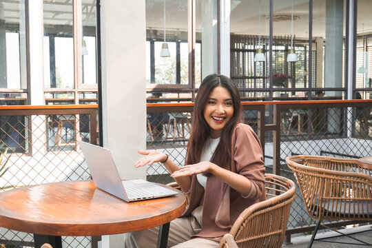 Smiling young Asian woman working remotely from cafe using her laptop, employee getting ready for online video-call interview