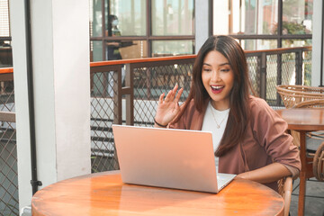 Young Asian woman doing video conference on laptop computer while sitting at the cafe, having meeting
