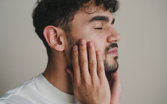Side view portrait of a handsome bearded man examining his face isolated over white background. Beauty care, skin problem treatment, skincare. Side view - Powered by Adobe