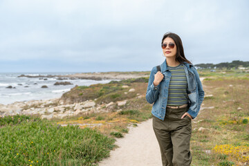 fashionable asian Japanese girl traveler walking leisurely along scenic California coastal beach...