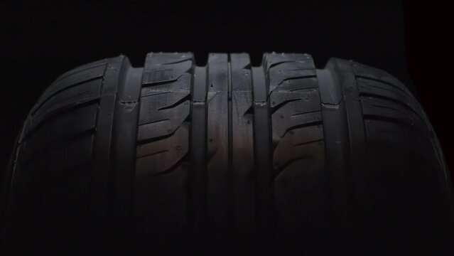 Slow Tire Rotation in the Dark. The new car tire is highlighted by a spotlight in the dark. The wheel rotates slowly toward the viewer against a black background