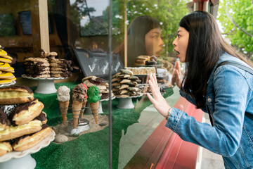 amazed asian Taiwanese girl keeping hand on display window and staring at mouthwatering desserts in a bakery while she visits Carmel by the sea in California usa