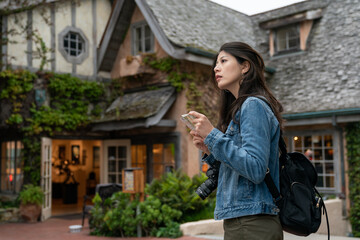 side portrait of asian korean girl backpacker looking into distance to check direction while consulting route map in Carmel by the sea against background of cozy fairytale hotel
