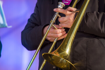 close-up of the hands of a street musician holding a gold-colored pump-action trumpet	