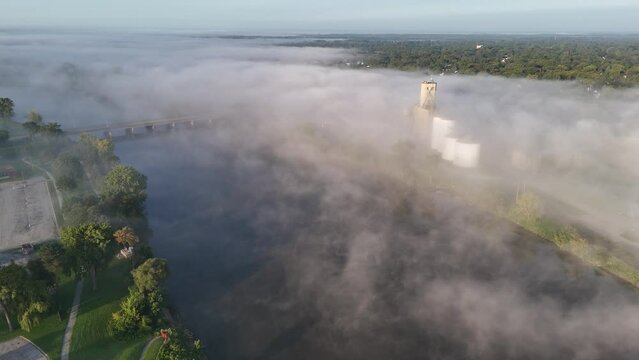 A foggy aerial view of the Saginaw River with silos peeking above the fog in the distance.  	