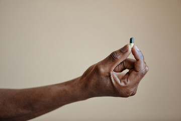 Closeup of Black male hand holding single capsule pill against neutral background, copy space