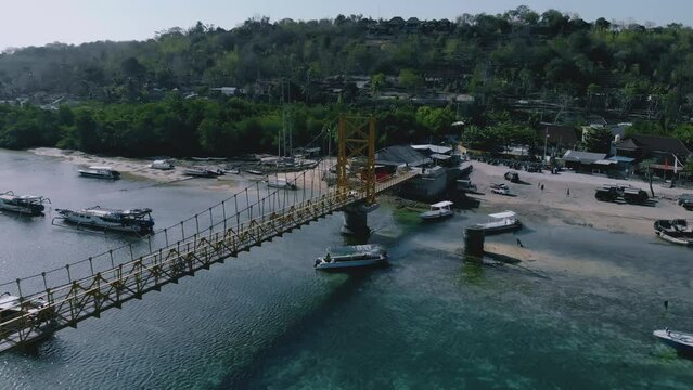 Aerial view of the yellow bridge which connect between Nusa Ceningan and Nusa Lembongan with boats anchored along the shore. Travel destination close to Bali island, Indonesia. 4K drone footage video