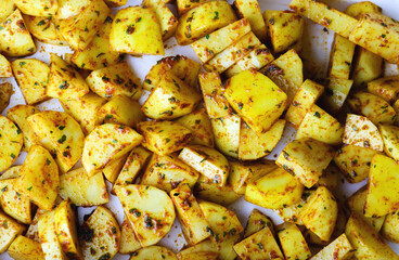 Raw potato slices in spices top view, close up. Fresh potato wedges mixed with herbs and spices ready to be baked or roasted. Raw potatoes with spices on a baking sheet ready to be cooked