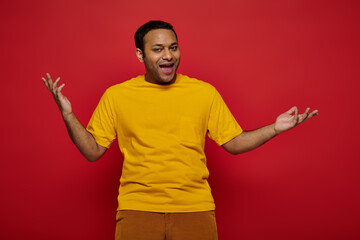 emotional indian man in bright casual clothes gesturing and talking on red background in studio