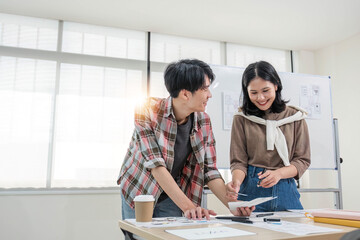 Obraz premium A smart and handsome young Asian male website developer is talking and planning a new project with a female colleague in the office. UI, UX, Tech Startup