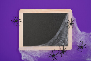 Blank black chalkboard with white cobwebs and black spiders on a purple background. A place for your text.