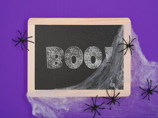 Black chalkboard with text boo, white cobwebs and black spiders on a purple background. A place for your text.