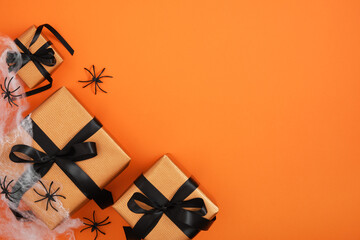 Orange gift boxes with black ribbons, white cobwebs and black spiders on orange background. A place...