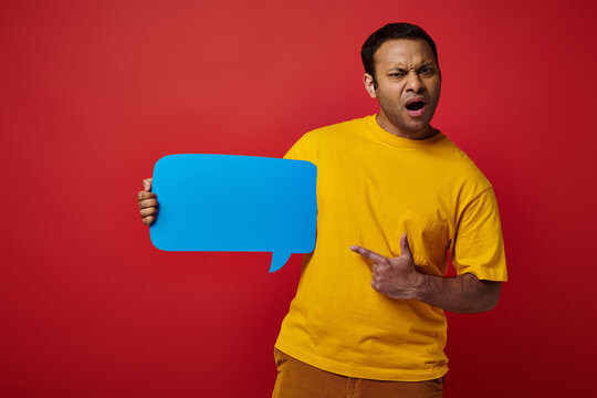 shocked man in yellow t-shirt pointing at blank speech bubble on red background, displeased