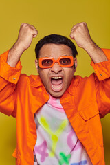 angry indian man in orange sunglasses looking at camera and gesturing on yellow background