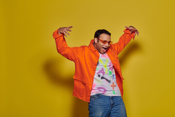 amazed indian man in sunglasses and vibrant attire looking down and gesturing on yellow background