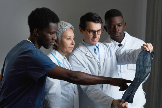 Young confident African American man in blue uniform pointing at x-ray image of patient while discussing it with group of colleagues at meeting