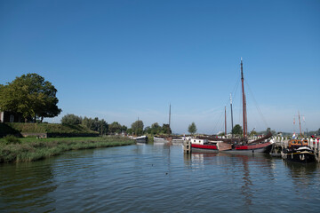 Fototapeta na wymiar Old sailing boats in the fortified Woudrichem city in The Netherlands, the harbor with a scenic rural typical Dutch landscape and sky in the Waal river on a cold winter day in North Brabant, Europe