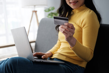 Smiling woman holding smartphone and banking credit card, involved in online mobile shopping at home, happy female shopper purchasing goods or services in internet