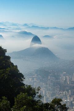 Rio de Janeiro, Brazil: city skyline, aerial view of the Guanabara bay with the Sugarloaf Mountain and Cable Car shrouded in fog in the early morning sunlight seen from Corcovado Mountain
