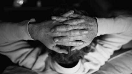 Back of senior man with hands clenched together in pensive mental reflection in monochrome black and white. Pensive elderly man detail hand