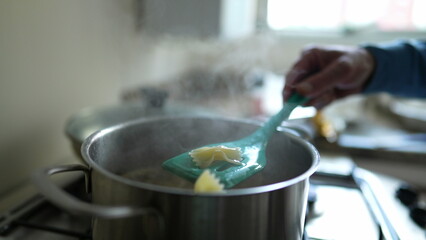 Close-up hand checking pasta inside metal pan to make sure it is al dente. Cooking carb food procedure on kitchen stove
