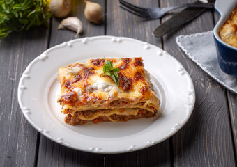 Portion of ground beef lasagna topped with melted cheese and garnished with fresh parsley served on a plate in close view for a menu