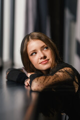 Portrait of an smiling teenage girl with her hands folded on the window sill.