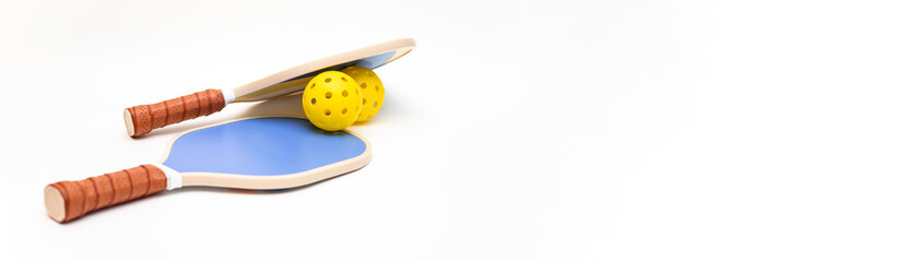 Composition of two pickleball rackets and two yellow balls on a white studio background with copy space. The paddles are on top of each other with the balls. Pickleball concept. Pickleball advertising