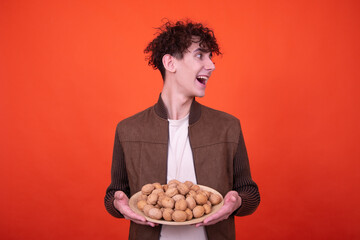 A young attractive guy eats walnuts. Funny man posing on an orange background.