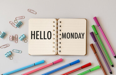 Message Hello Monday written in notebook, computer keyboard and colorful markers and paper clips white desk, flat lay