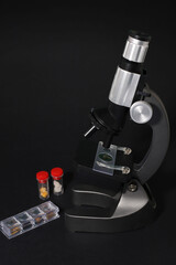 black metal microscope on a dark background. test tubes with a red cap next to them