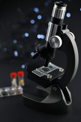 black metal microscope on a dark background. test tubes with a red cap next to them