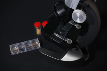 black metal microscope on a dark background. test tubes with a red cap next to them