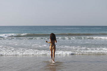 Happy bikini beach vacation woman running to ocean water in freedom feeling. Happiness carefree lifestyle photo with sea and sky copy space.