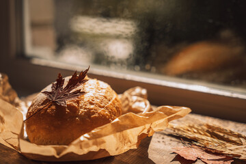 Fresh loaf of bread in paper packaging with maple leaves in front of the window.