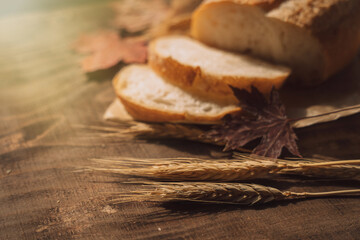 Sliced fresh loaf of bread in paper packaging with ears of wheat and maple leaves on a wooden table.