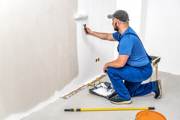 Builder painting the wall with painting roller in white color - obrazy, fototapety, plakaty