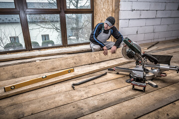 Carpenter works with wooden board. Mitre saw