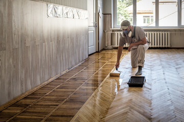 Worker uses a roller to coating floors. Varnishing lacquering parquet floor by paint roller