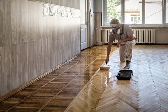 Worker uses a roller to coating floors. Varnishing lacquering parquet floor by paint roller
