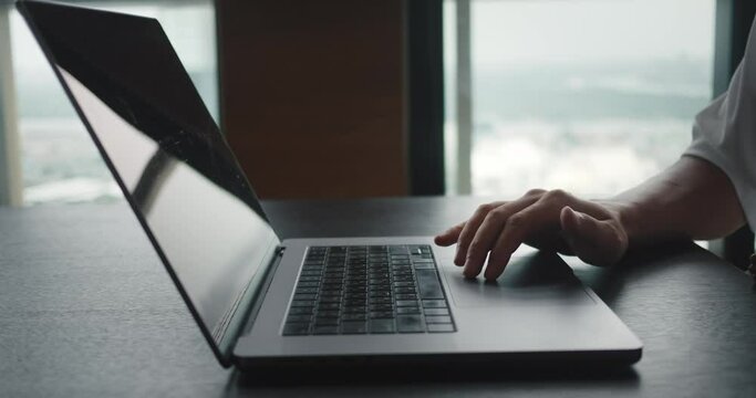 Successful Businessman Sitting At Desk Working At Laptop In Office. Business Person Using Touch Pad Laptop Computer In Front Of Window At Office