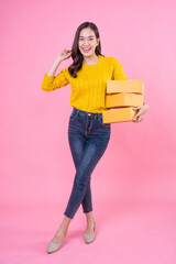 Happy asian woman smiling and holding package parcel box isolated on pink background. Carry delivery goods. Delivery courier and shipping service concept. 