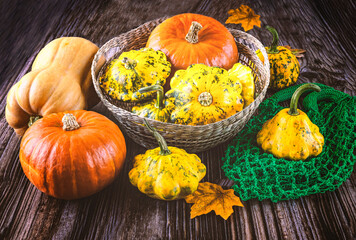Harvest of ripe yellow and orange pumpkins in basket, autumn leaves, knitted green bag on wooden...