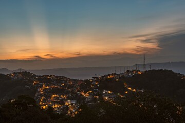 Naklejka premium City of Santos, Brazil. Sunset at Saboó Hill. Neighborhood and illuminated streets. In the background the mountains of the Serra do Mar.