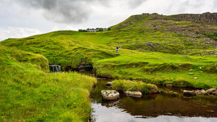 Woman hiking through a green meadow with waterfalls on the Isle of Skye, Scotland.