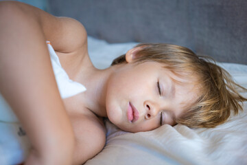 Obraz na płótnie Canvas Portrait of a sleeping little boy with golden hair on a white bed