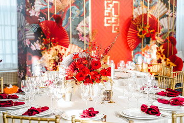 Floral arrangement, festive bouquet, table decoration for Chinese New Year party celebration in restaurant. Traditional red gold color decor. Roses,poppies,fan,candles,tassels. Chinese lunar calendar